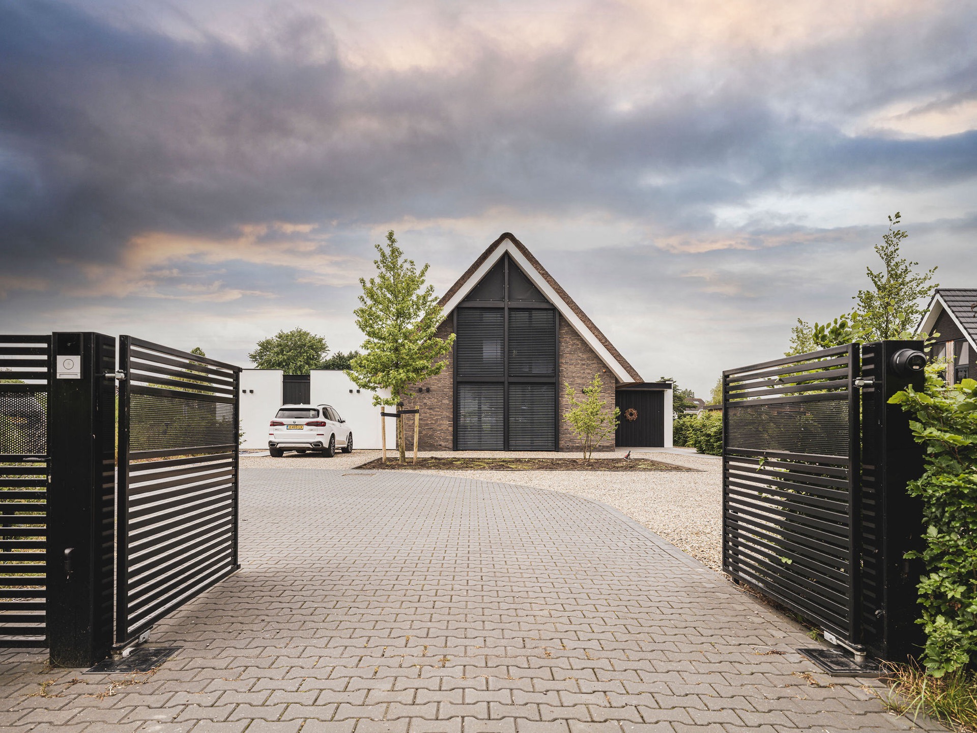 Villa mit Reetdach und Giebel: einfahrt mit schwarzem Tor und Blick auf den reetgedeckten Giebel mit Lamellenfenstern, Luxury, Design, Exclusive, Modern, Custom Made, Special, Beautiful
