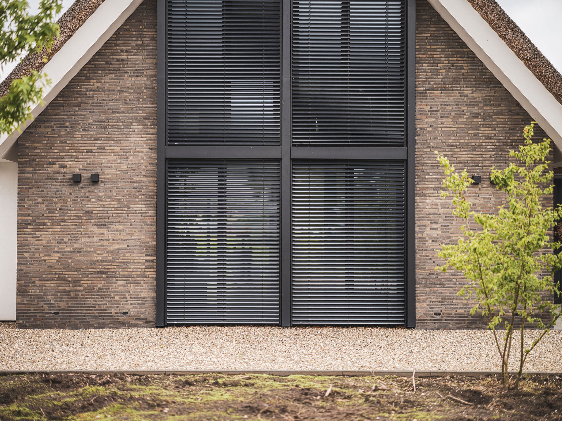 Villa mit Reetdach und Giebel: detailaufnahme: dunkle Lamellenfenster in Ziegelwand unter reetgedecktem Dachrand, Luxury, Design, Exclusive, Modern, Custom Made, Special, Beautiful