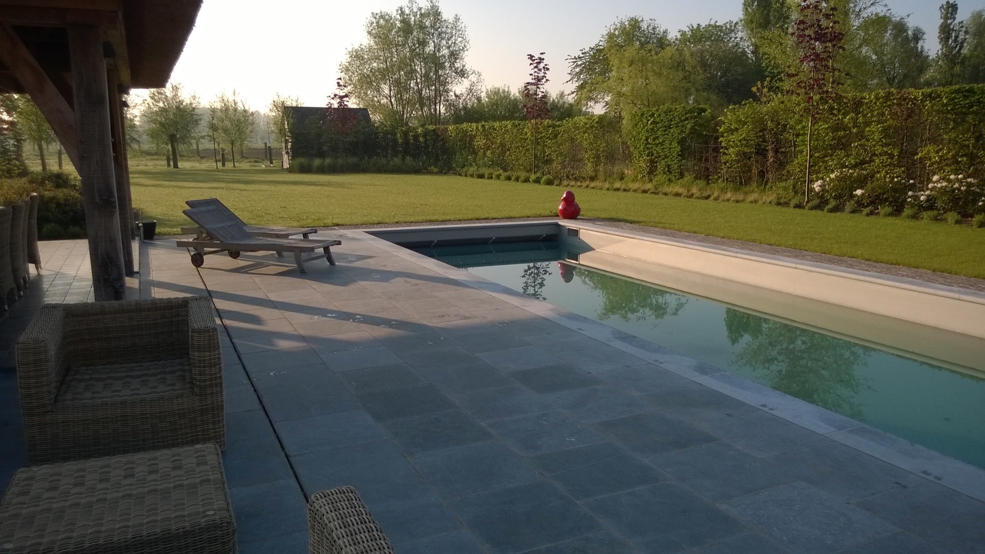 piscina en el jardín: vista a lo largo de la piscina con pavimento de piedra natural y caseta de jardín de techo de paja en, Luxury, Design, Exclusive, Modern, Custom Made, Special, Beautiful