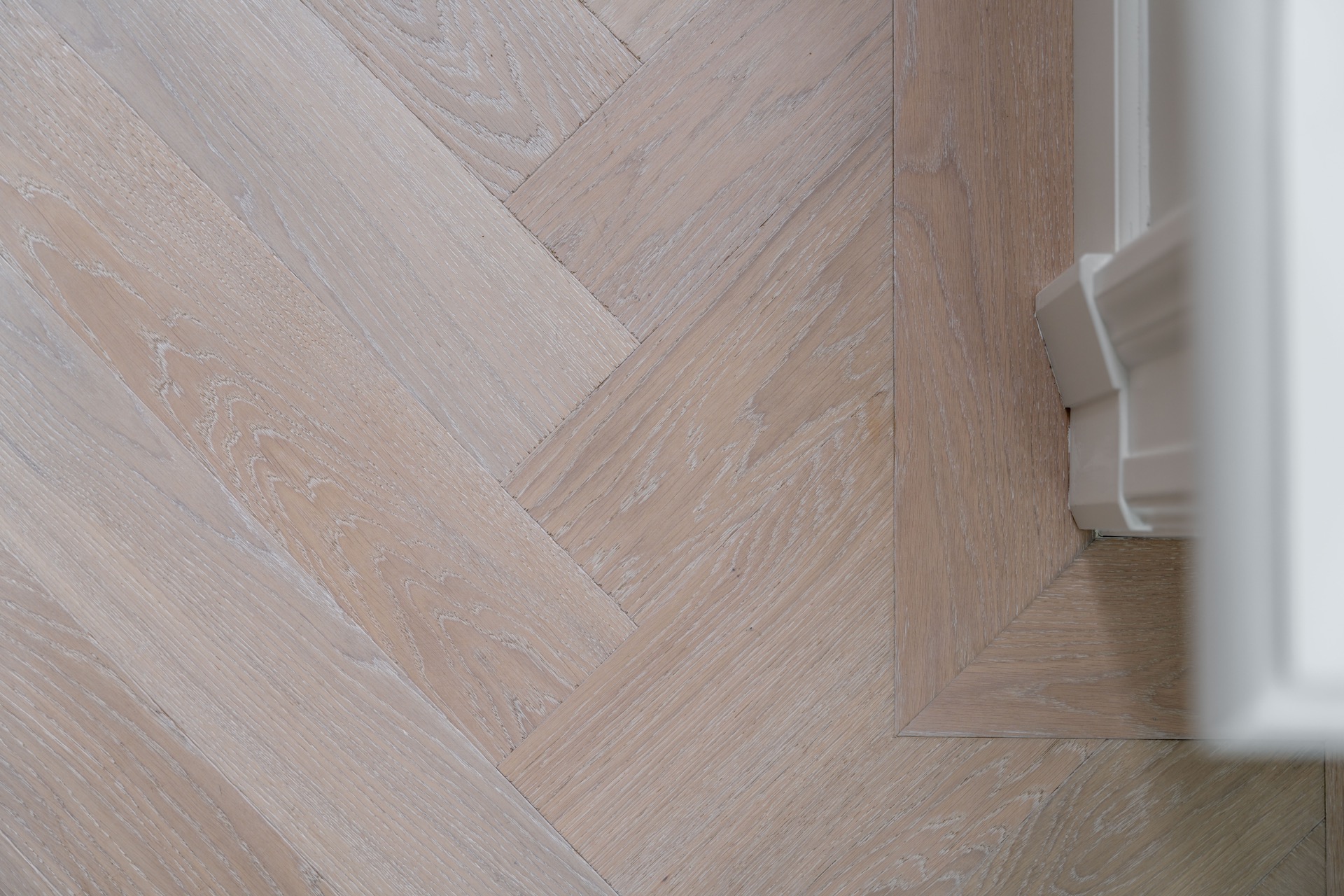parquet en chevron chêne blanc: gros plan sur un parquet herringbone en chêne clair à finition blanc-gris et plinthe nette, Luxury, Design, Exclusive, Modern, Custom Made, Special, Beautiful