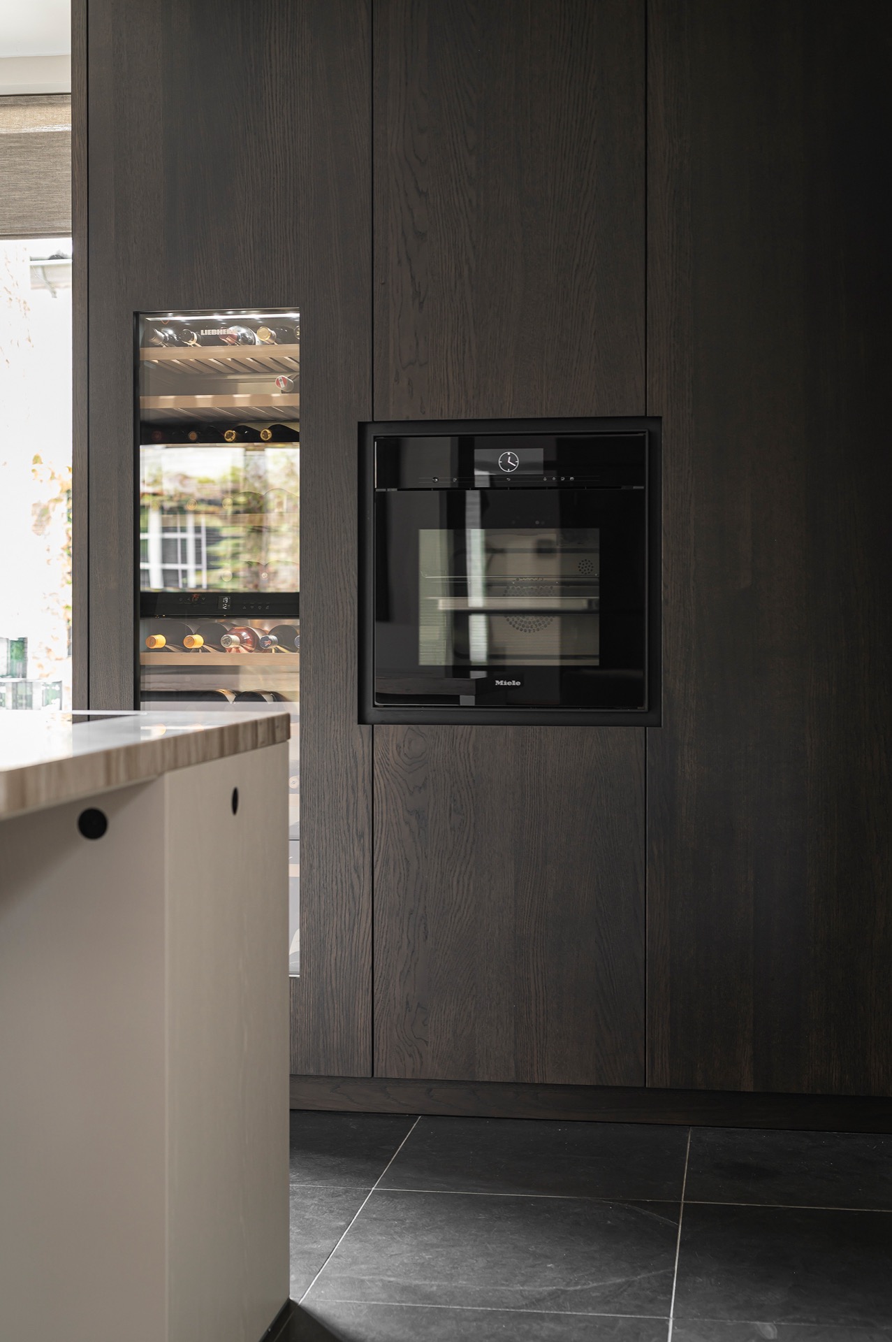 cucina senza maniglie con isola e angolo caffè: parete di armadi scuri con elettrodomestico integrato e parte in vetro in, Luxury, Design, Exclusive, Modern, Custom Made, Special, Beautiful
