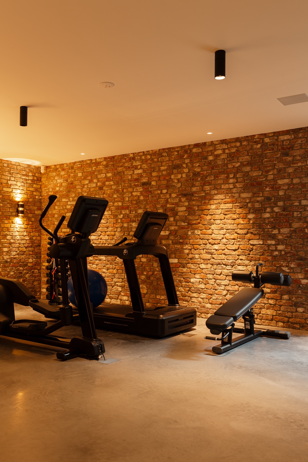 floated concrete floor in new-build villa: fitness room with brick wall, floated concrete floor and warm lighting, Luxury, Design, Exclusive, Modern, Custom Made, Special, Beautiful