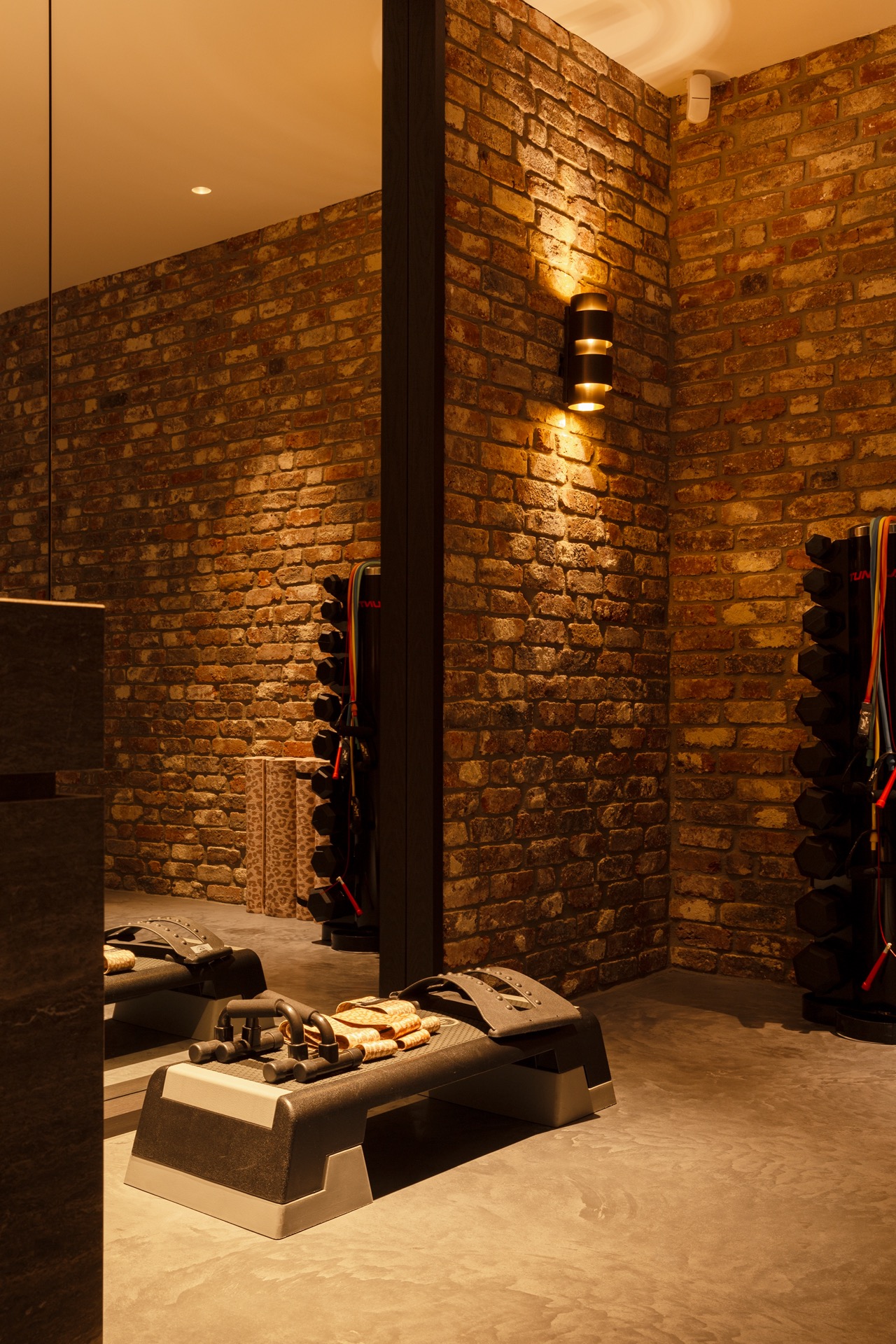 floated concrete floor in new-build villa: part of fitness room with brick wall and wall lights with warm glow, Luxury, Design, Exclusive, Modern, Custom Made, Special, Beautiful