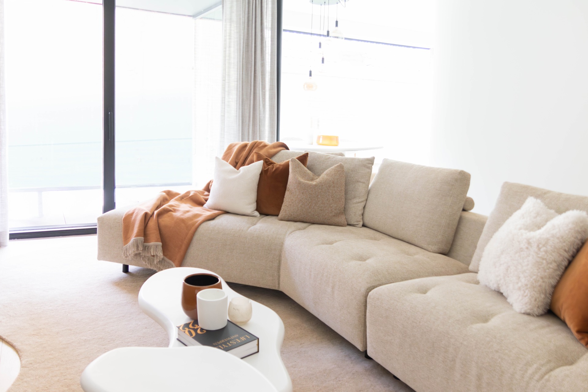 interno minimalista caldo su misura: soggiorno luminoso con divano ad angolo beige, cuscini e tende davanti a una grande, Luxe, Design, Exclusief, Modern, Maatwerk, Bijzondere, Mooie