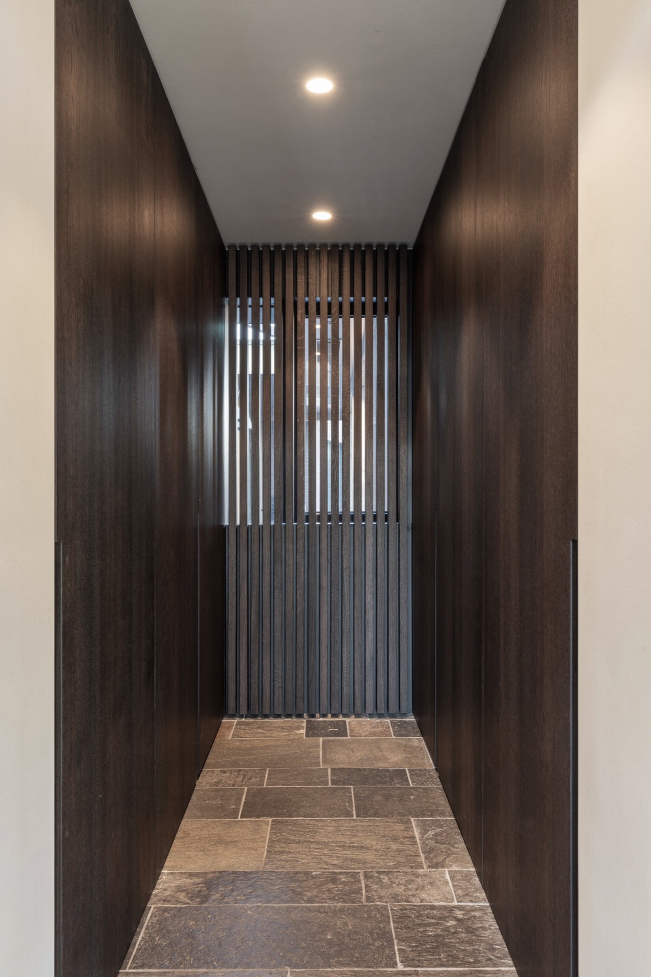 interni minimal caldi con legno e pietra: corridoio stretto con parete a doghe in legno scuro, pavimento in piastrelle e, Luxury, Design, Exclusive, Modern, Custom Made, Special, Beautiful