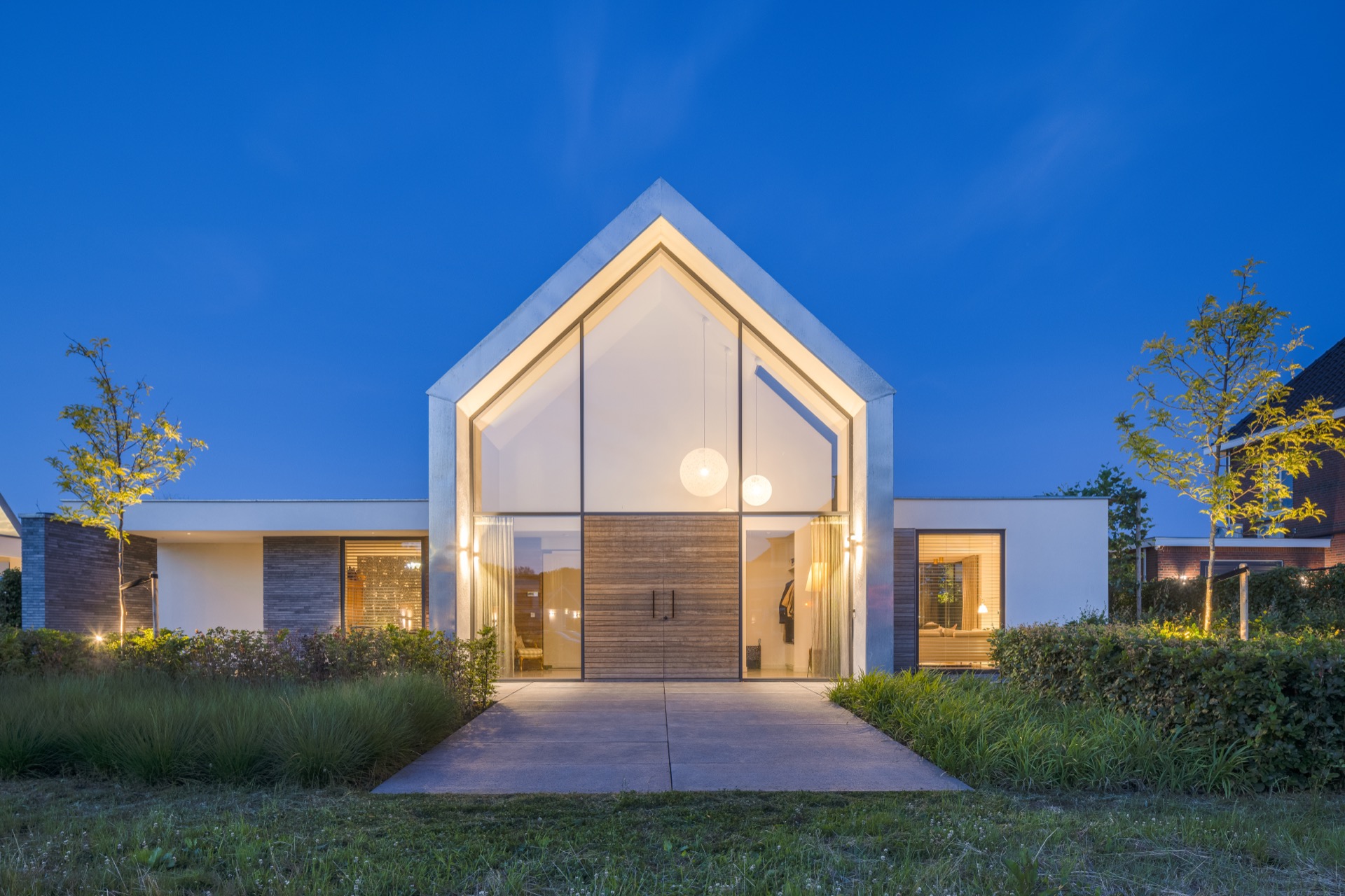 villa con accento facciata tipo zinco: facciata anteriore di notte con ingresso illuminato, lamelle sopra l’apertura in, Luxe, Design, Exclusief, Modern, Maatwerk, Bijzondere, Mooie