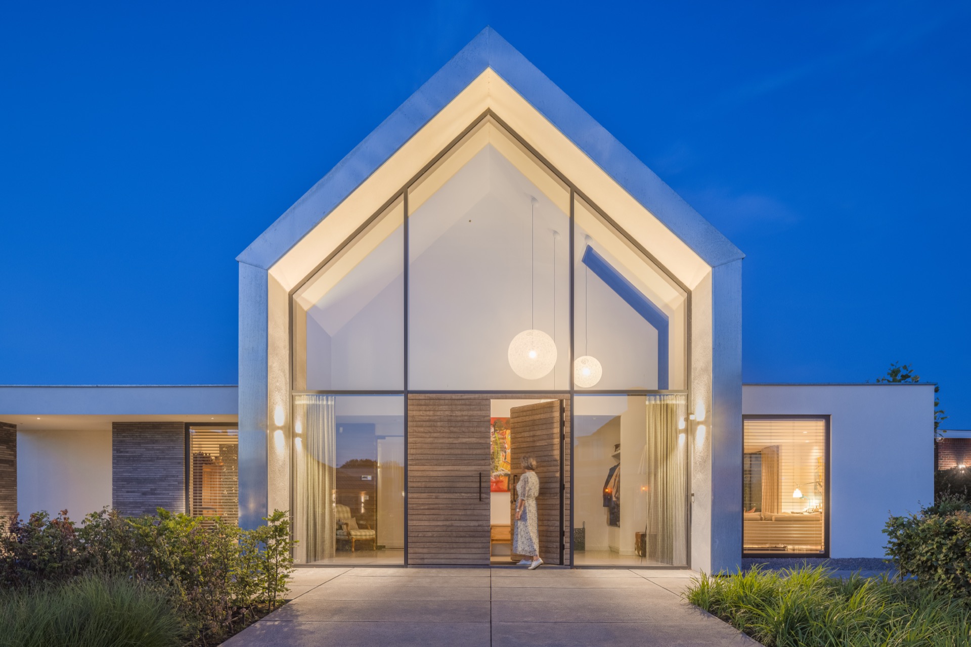 villa con accento facciata tipo zinco: dettaglio notturno dell’ingresso: interno illuminato visibile attraverso il vetro e, Luxe, Design, Exclusief, Modern, Maatwerk, Bijzondere, Mooie
