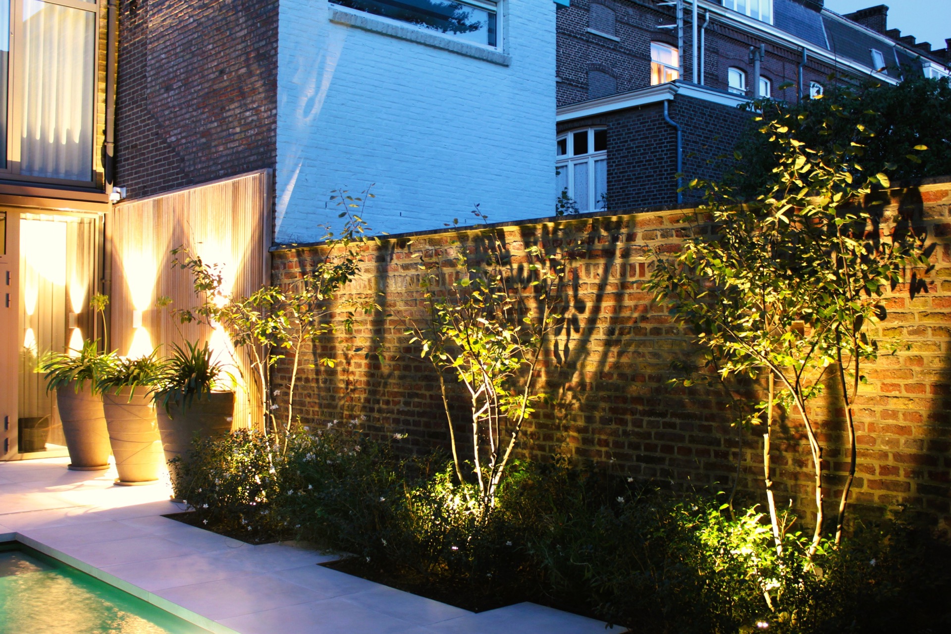 pool lounge area: evening view of patio garden with illuminated plants in planters, brick wall and ceramic tiled terrace, Luxury, Design, Exclusive, Modern, Custom Made, Special, Beautiful