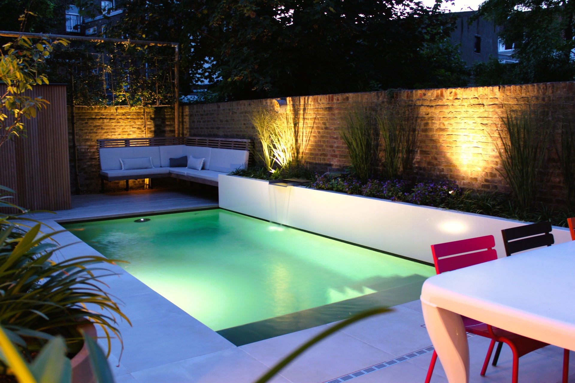 pool lounge area: night view of patio garden with illuminated pool, lounge bench and warm lighting on brick wall, Luxury, Design, Exclusive, Modern, Custom Made, Special, Beautiful