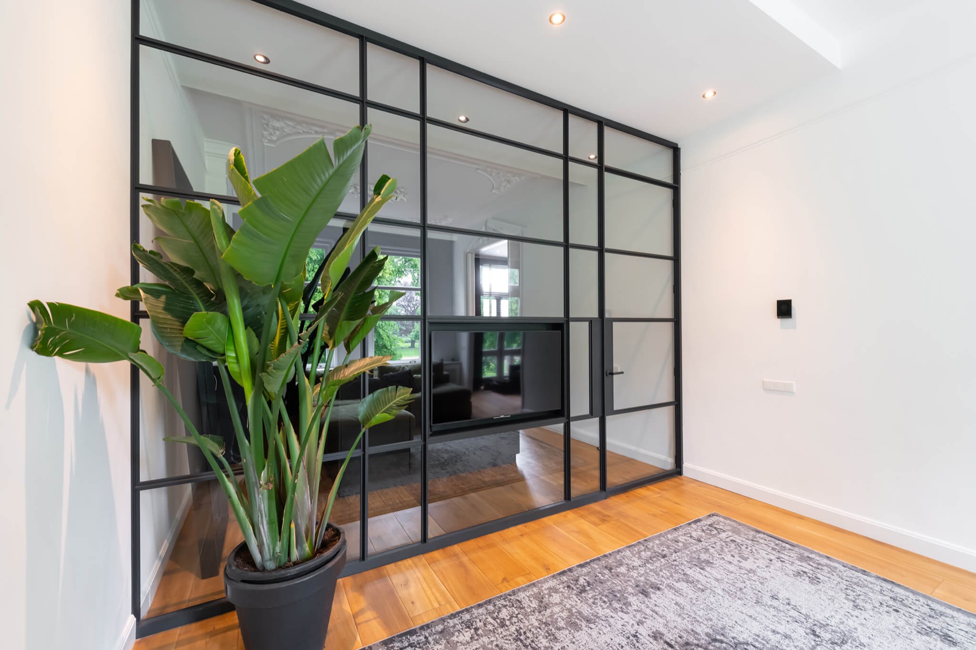 glass TV wall with hinged door: detail of a glass cinewall with a black aluminum door frame and grid panels, Luxury, Design, Exclusive, Modern, Custom Made, Special, Beautiful