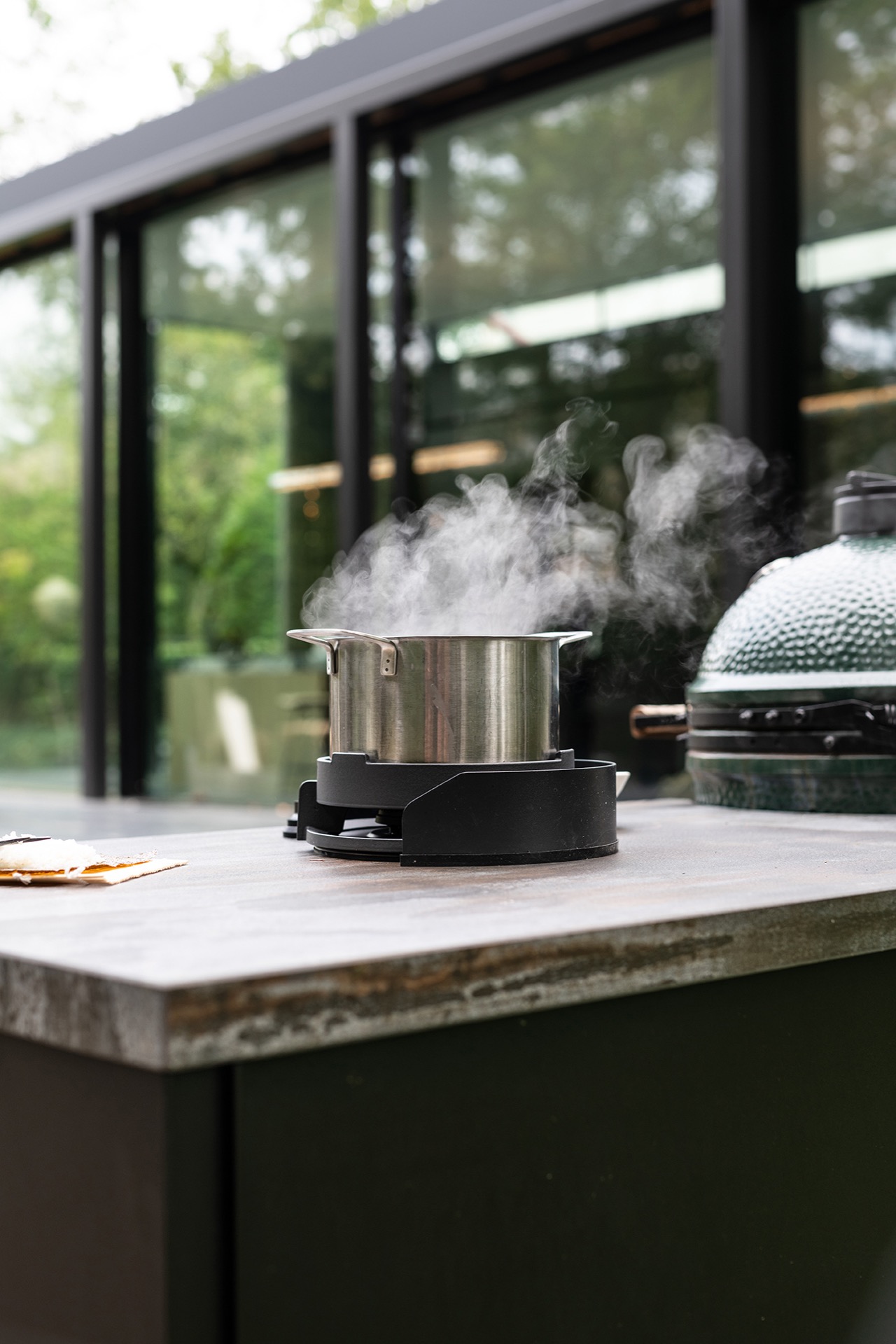 modern outdoor kitchen with natural stone worktop: cooking pot with steam on an outdoor kitchen countertop under a glass wall, Luxury, Design, Exclusive, Modern, Custom Made, Special, Beautiful