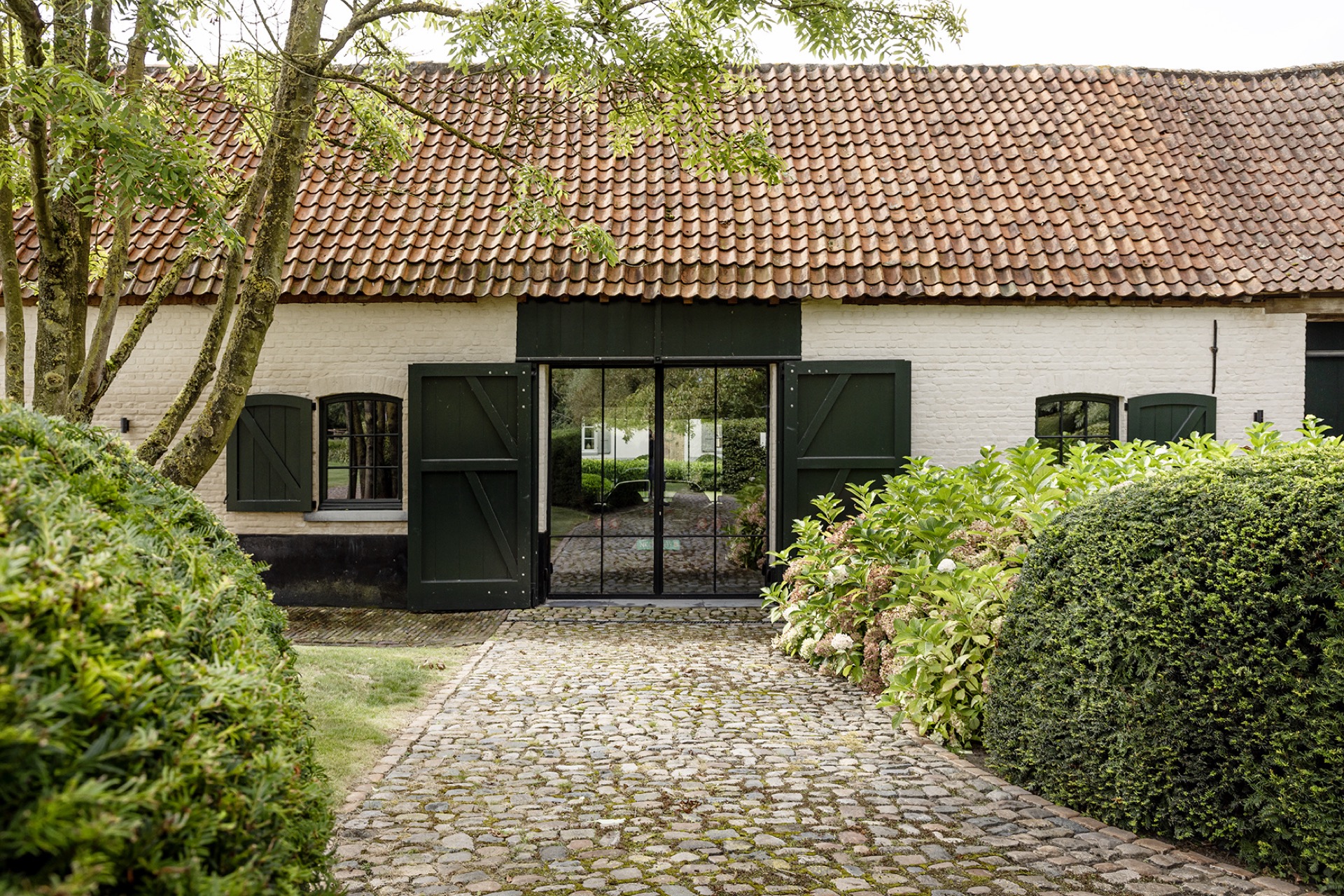 landscape garden sightline: dark doors and large glazed opening in a white outbuilding facade with cobblestone path, Luxury, Design, Exclusive, Modern, Custom Made, Special, Beautiful