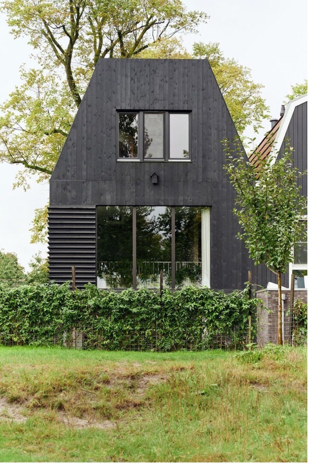 indoor-outdoor connection home: rear facade with black timber cladding and large windows along a green garden edge, Luxe, Design, Exclusief, Modern, Maatwerk, Bijzondere, Mooie
