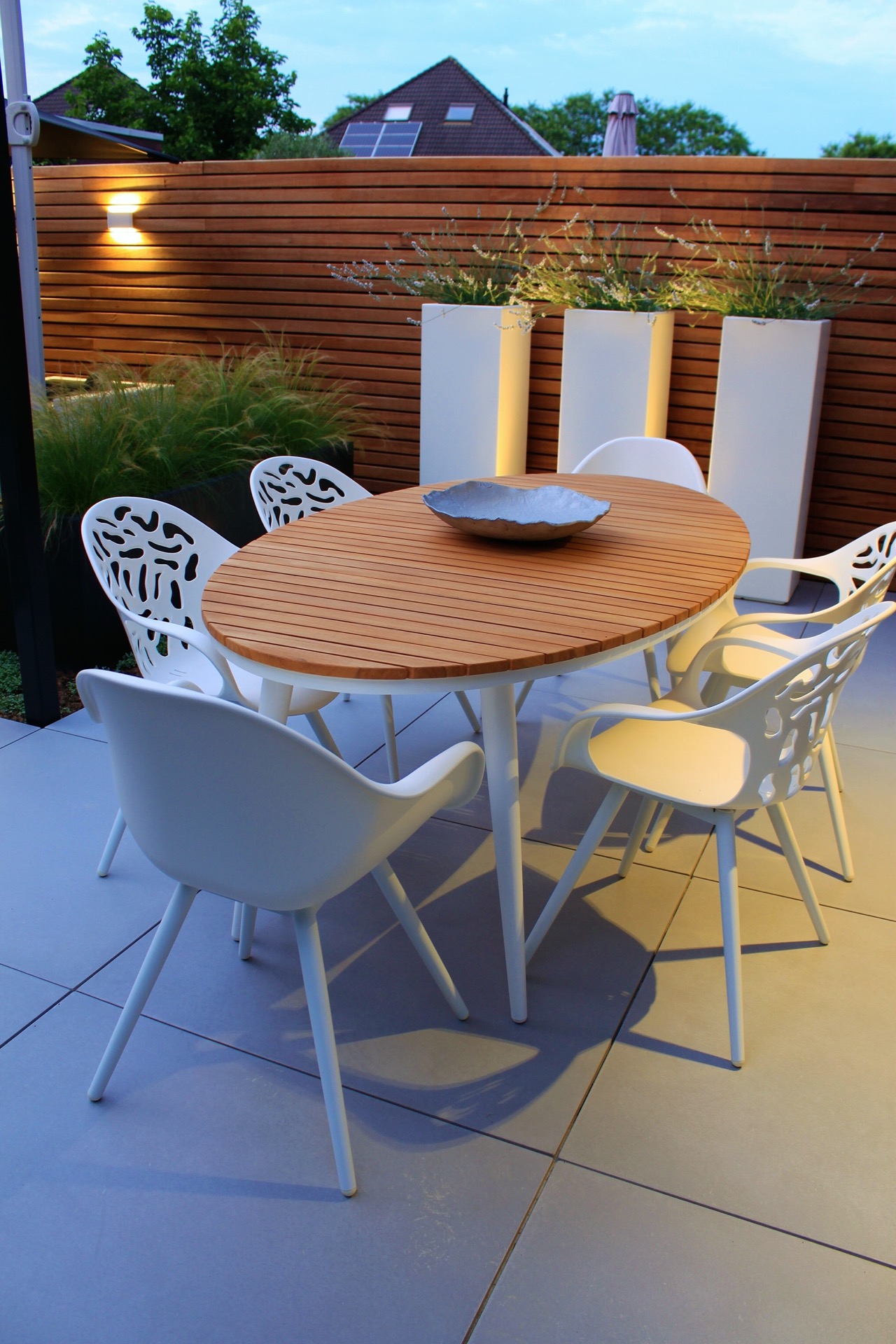 giardino moderno: tavolo da pranzo rotondo con sedie bianche su terrazza piastrellata vicino a fioriere alte e parete a, Luxury, Design, Exclusive, Modern, Custom Made, Special, Beautiful