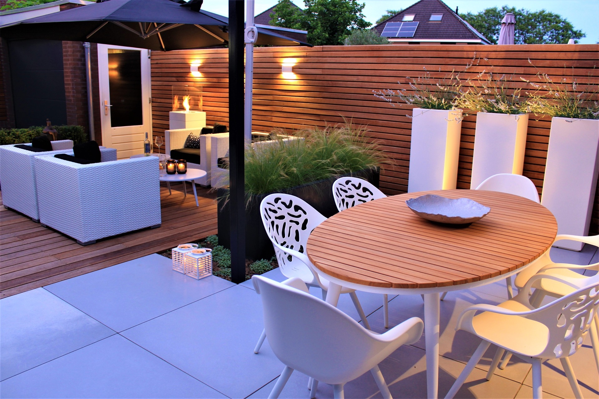 jardín moderno: mesa redonda de madera sobre terraza de baldosas con zona de estar y pared de lamas iluminada al fondo, Luxury, Design, Exclusive, Modern, Custom Made, Special, Beautiful