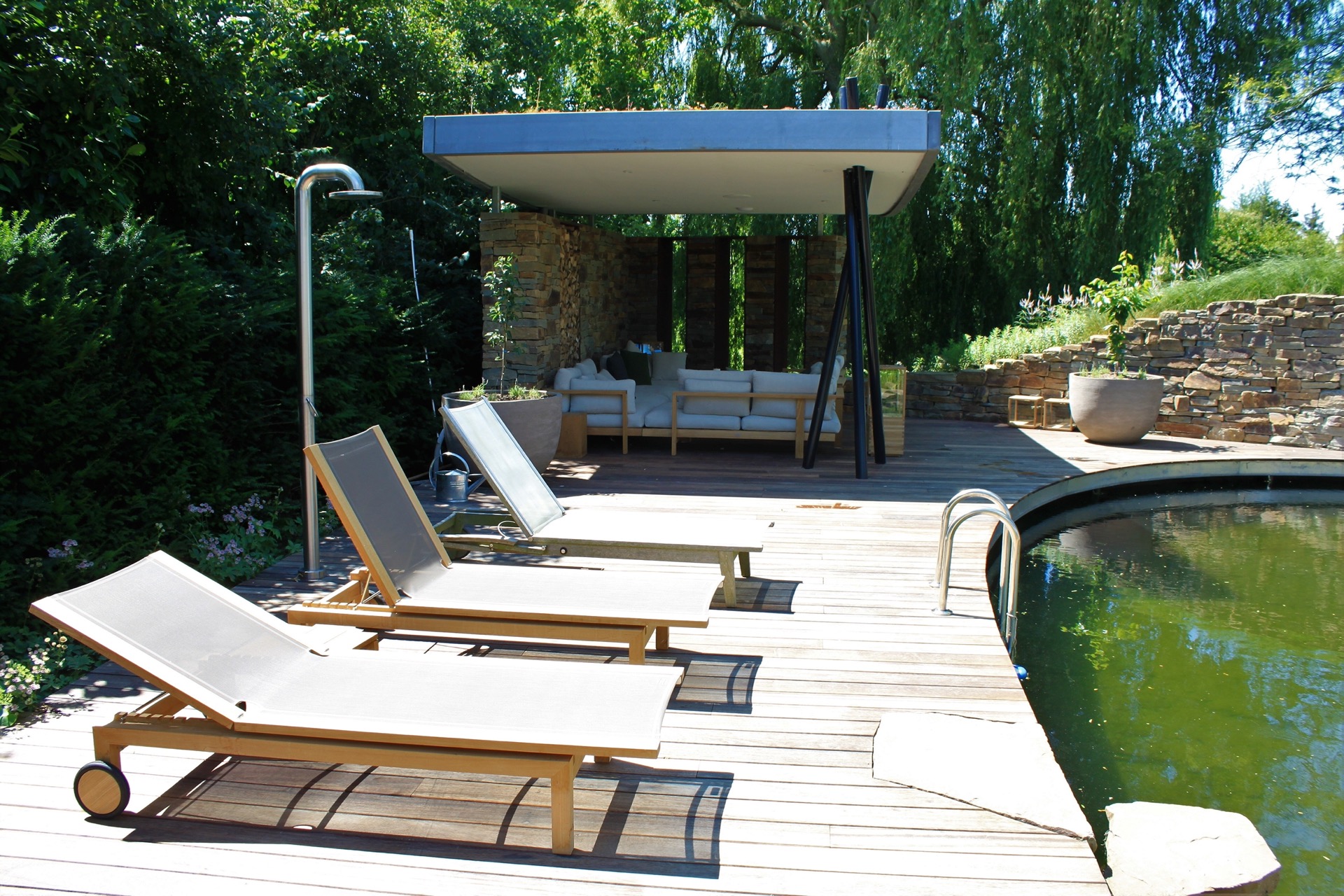 vasca da nuoto naturale con cascata: lettini e terrazza in legno vicino a una vasca da nuoto con cascata in una parete in, Luxury, Design, Exclusive, Modern, Custom Made, Special, Beautiful