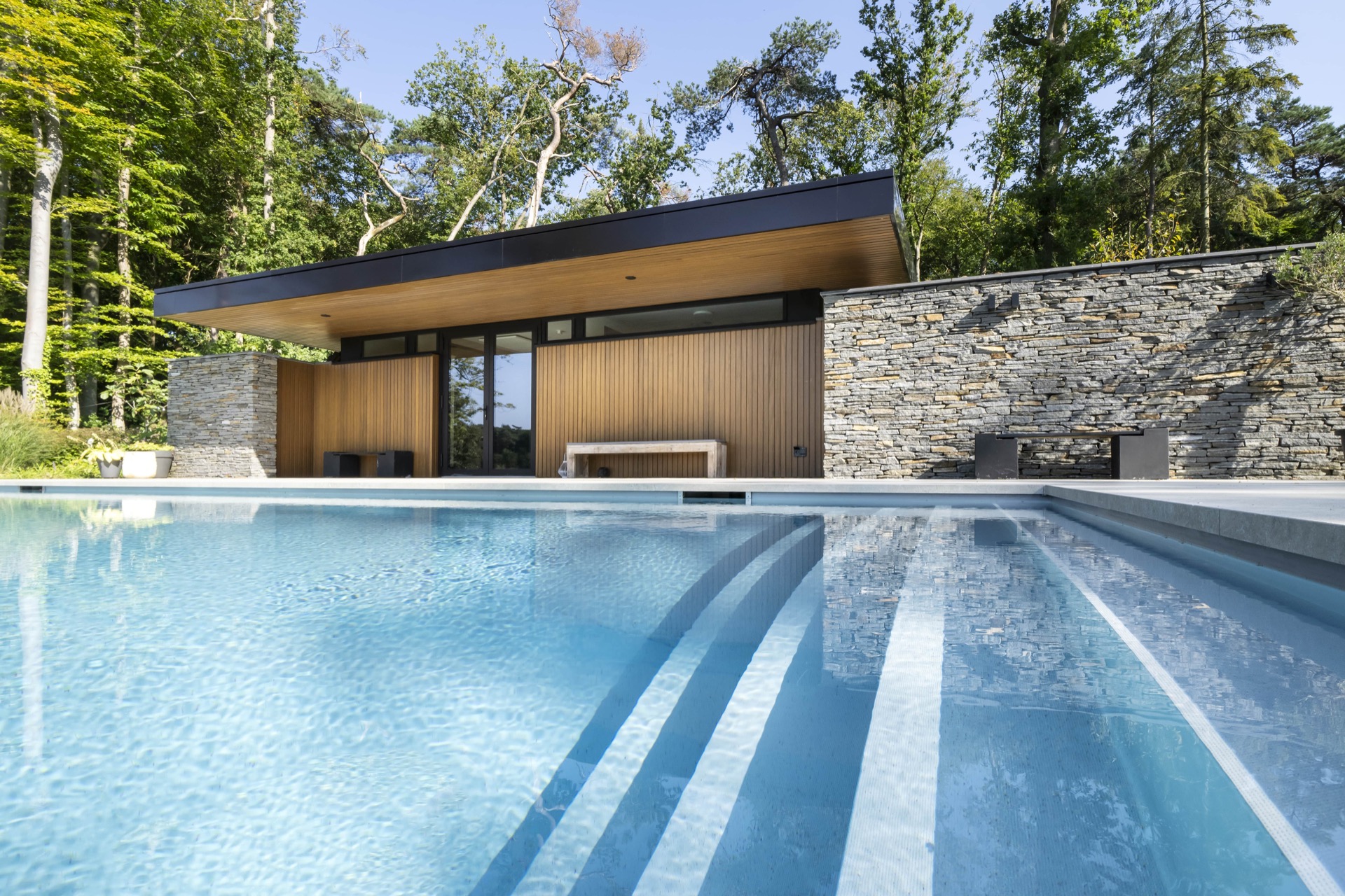 piscina skimmer rivestimento grigio chiaro: vista frontale della piscina con pannelli in legno e muro in pietra naturale in, Luxury, Design, Exclusive, Modern, Custom Made, Special, Beautiful