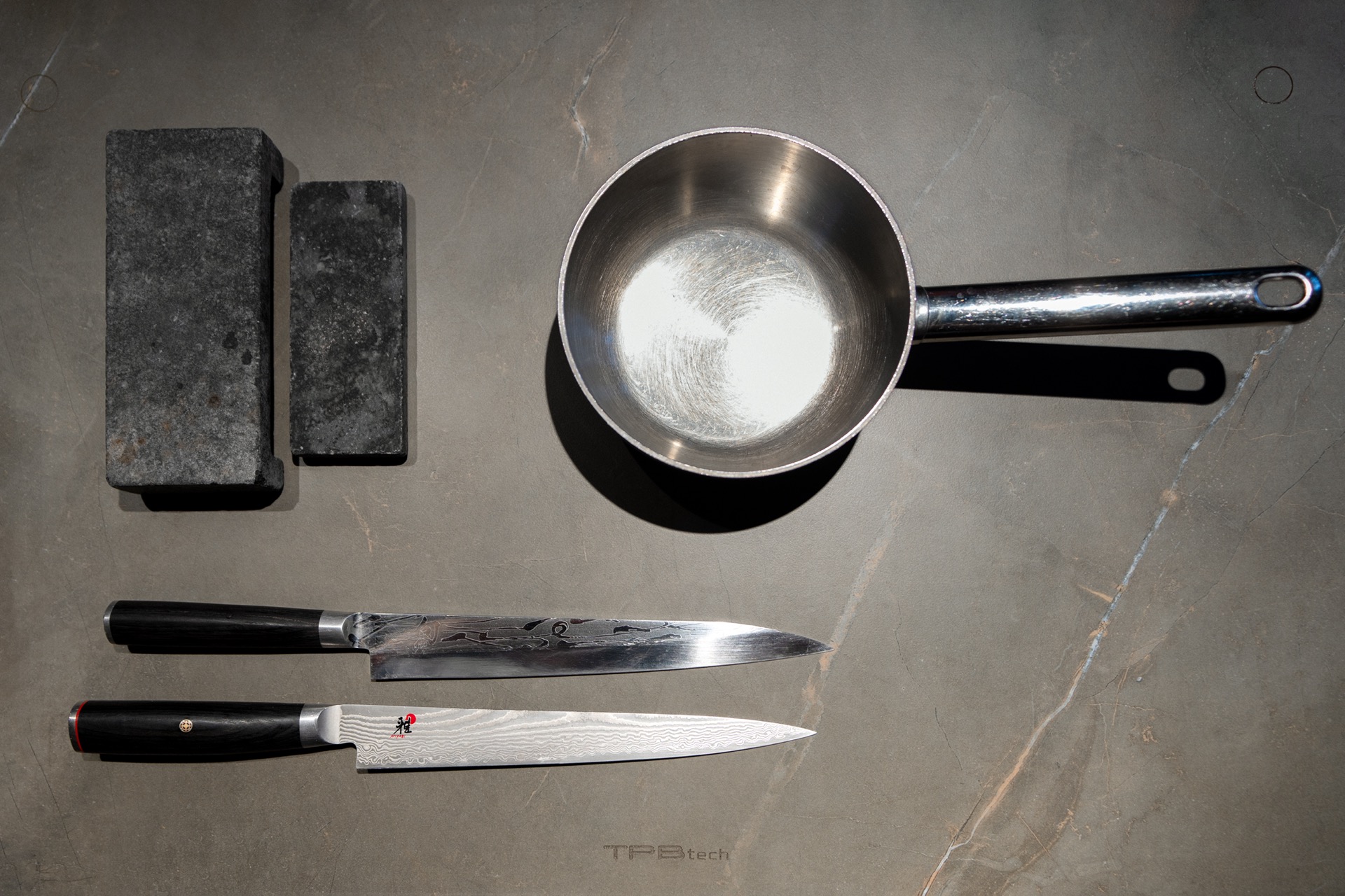 cucina chef’s table con induzione invisibile: dettaglio: padella e blocchi di pietra scura sul piano di lavoro della chef’s, Luxury, Design, Exclusive, Modern, Custom Made, Special, Beautiful