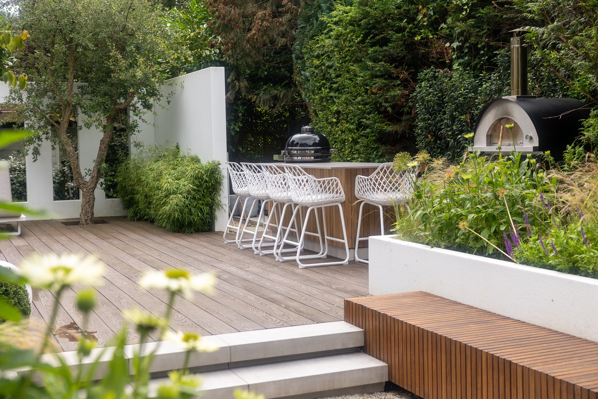 cucina esterna legno: terrazza in legno con sgabelli da bar in metallo bianco e piante verdi lungo muro esterno bianco, Luxury, Design, Exclusive, Modern, Custom Made, Special, Beautiful