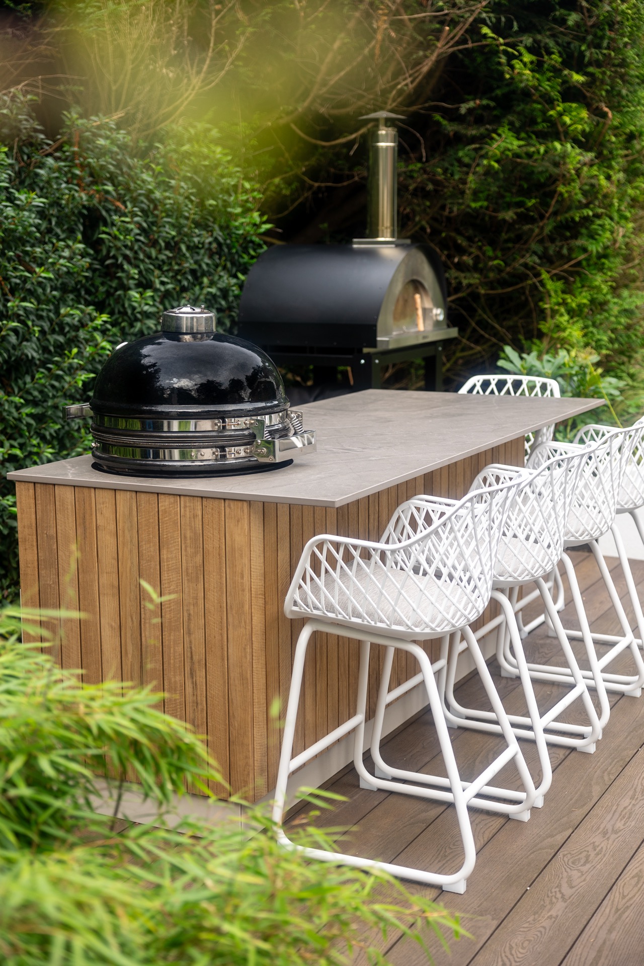 cucina esterna legno: bar esterno con listelli in legno, griglia in ceramica e forno a legna in giardino con sgabelli bianchi, Luxury, Design, Exclusive, Modern, Custom Made, Special, Beautiful
