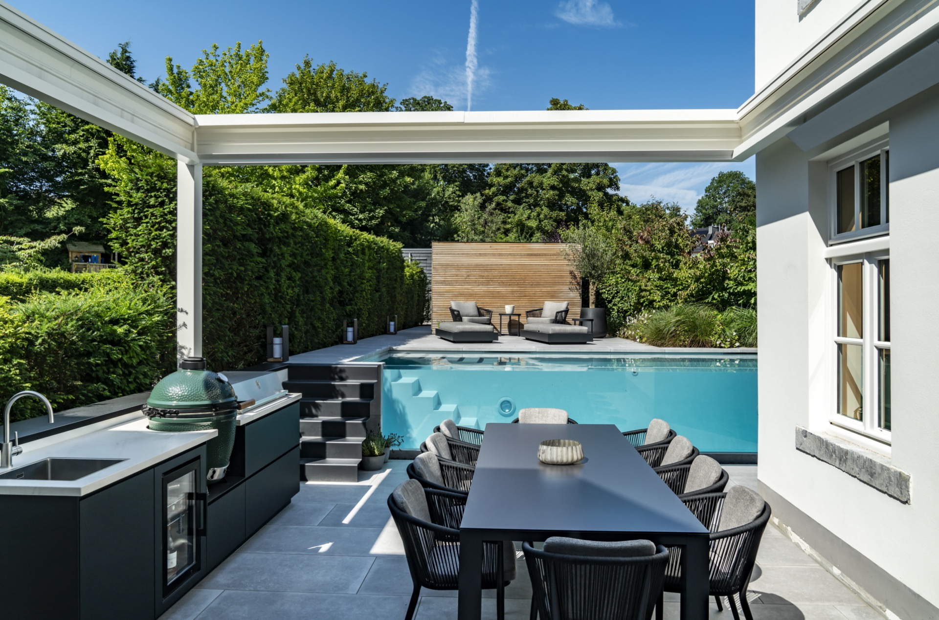 piscina con parete in vetro: piscina esterna con parete di vetro, cucina esterna nera e sedie grigie al tavolo da pranzo, Luxury, Design, Exclusive, Modern, Custom Made, Special, Beautiful