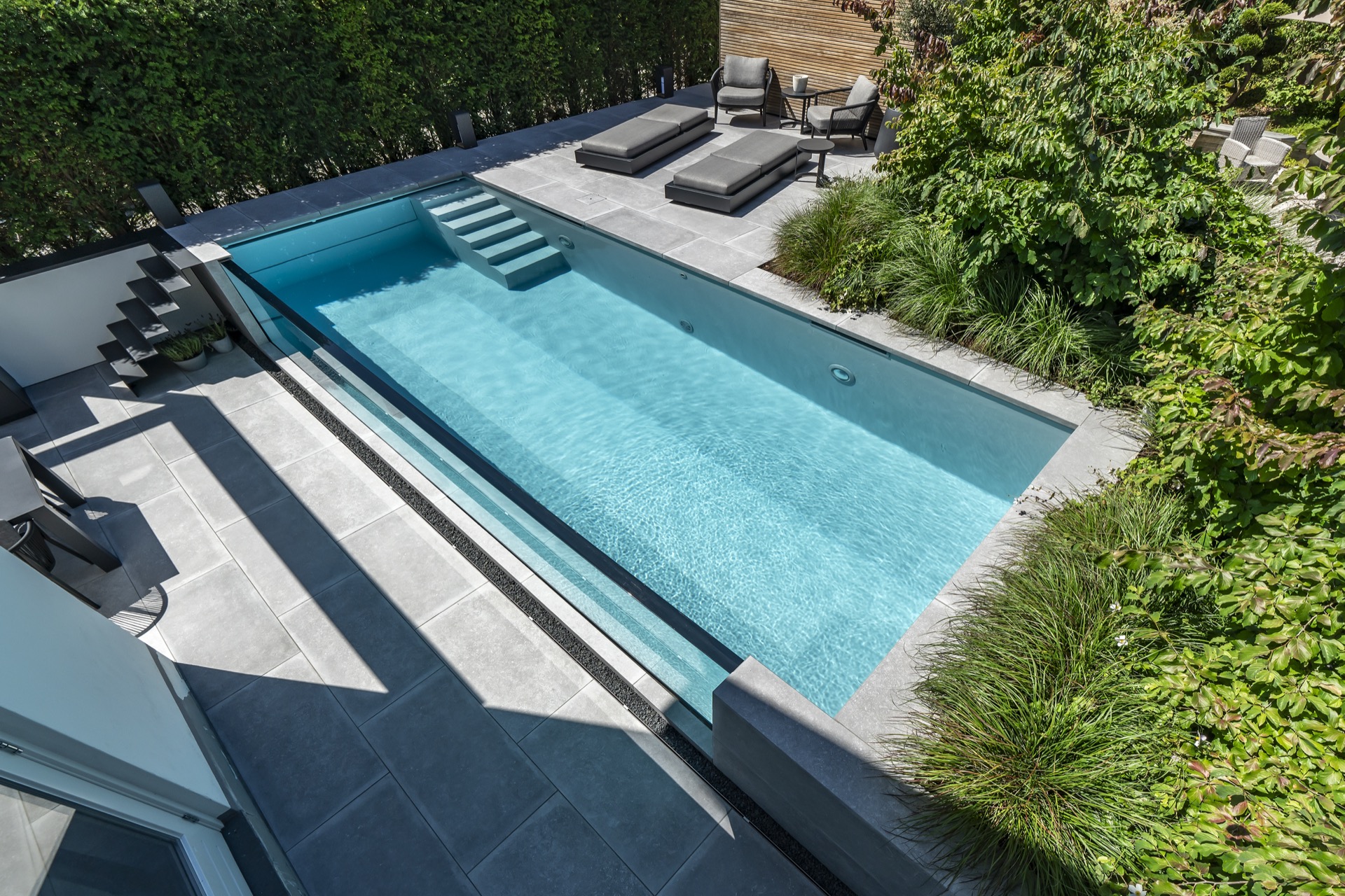 piscina con parete in vetro: vista piscina moderna con parete di vetro, lettini grigi e parete in legno, Luxury, Design, Exclusive, Modern, Custom Made, Special, Beautiful