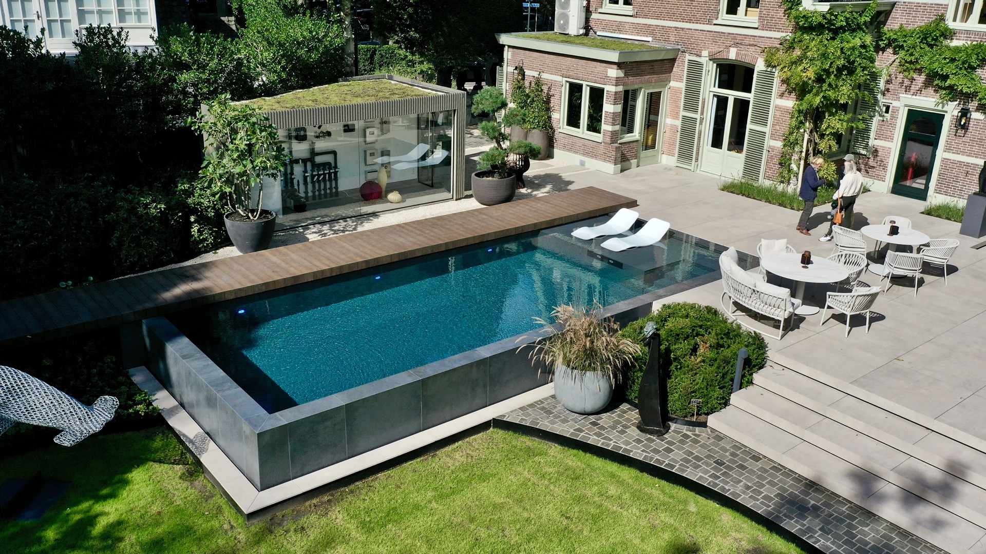 locale tecnico piscina fuori terra: piscina a sfioro con terrazza in legno e locale tecnico in vetro vicino a villa classica, Luxury, Design, Exclusive, Modern, Custom Made, Special, Beautiful